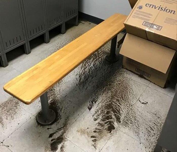 Raw sewage in tile floor with lockers, a wooden bench and empty boxes