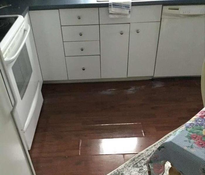 Standing water in kitchen next to white kitchen cabinets, with oven and sink