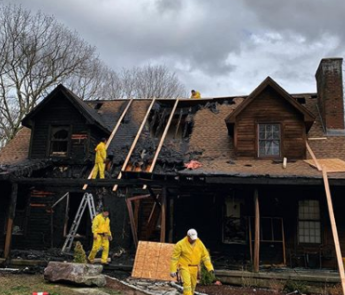 two story house damaged by fire with three workers cleaning debris