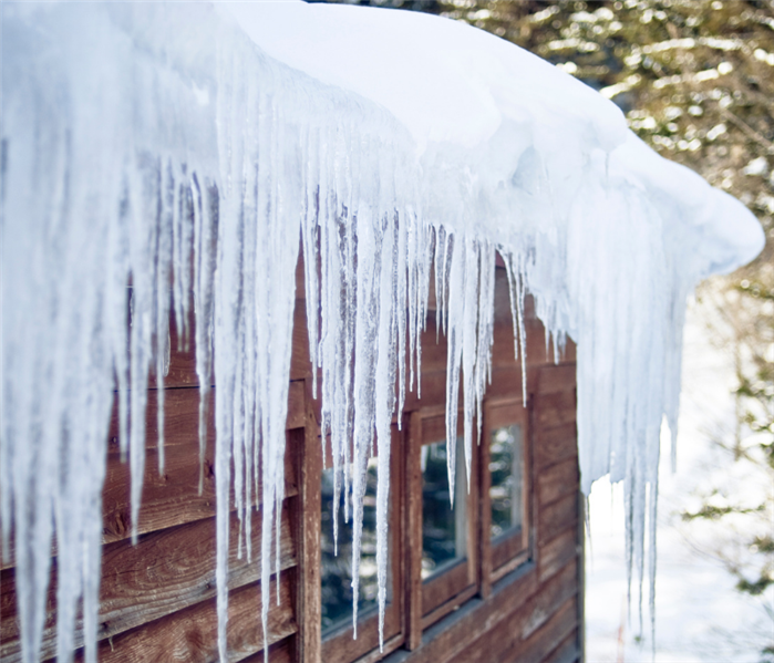photo of ice dam forming on the edge of roof of log cabin, large icicles hanging down