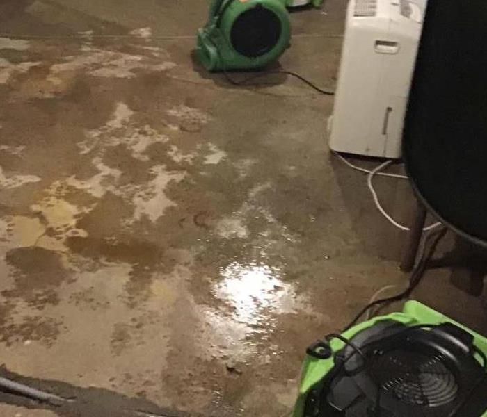 wet unfinished concrete basement floor with SERVPRO fan blower, washer, dehumidifier & shelf